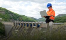 Специалист работает за ноутбуком рядом с плотиной ГЭС